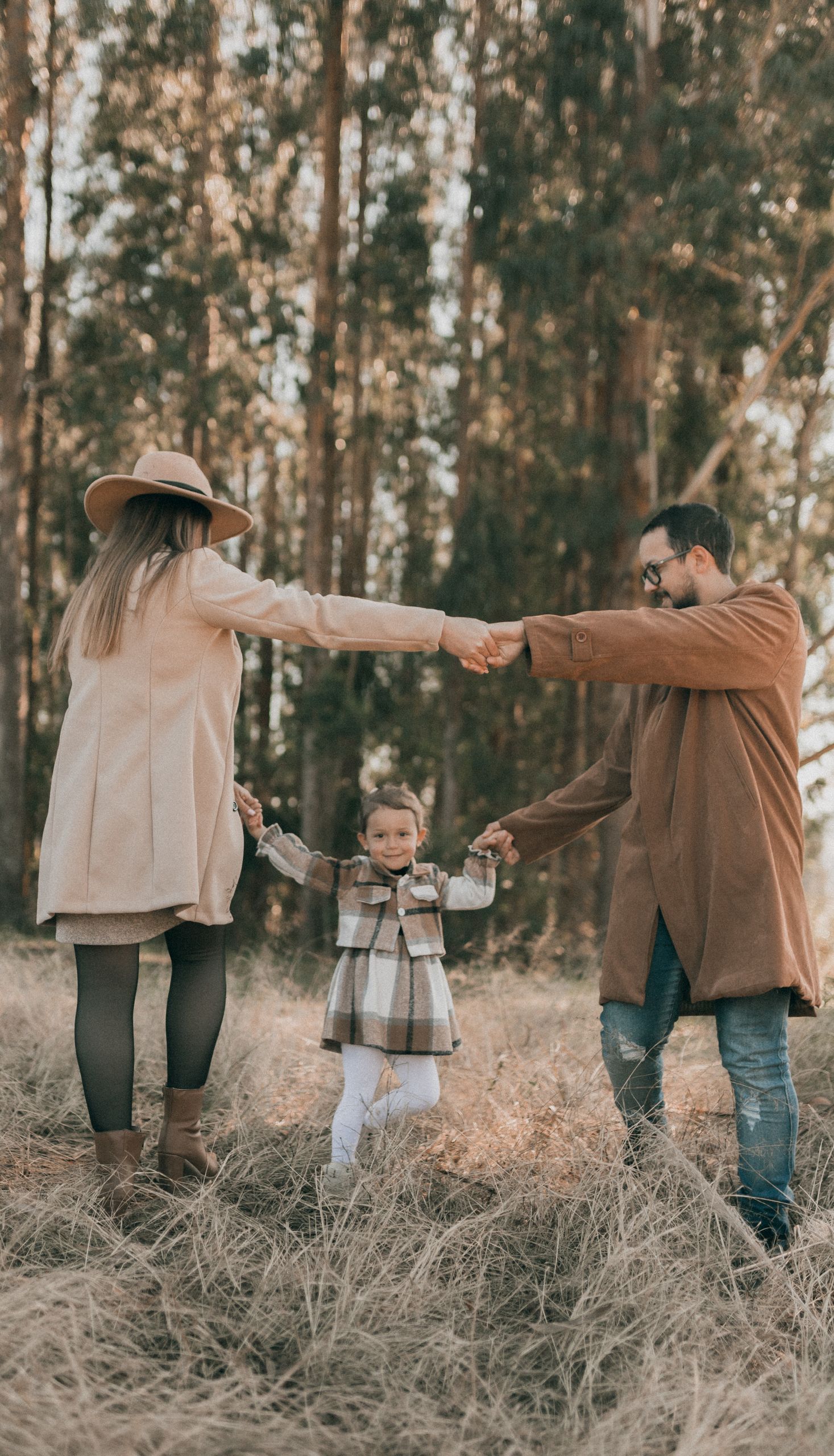 Happy family with child enjoying a sunny autumn day in the forest, holding hands and smiling.